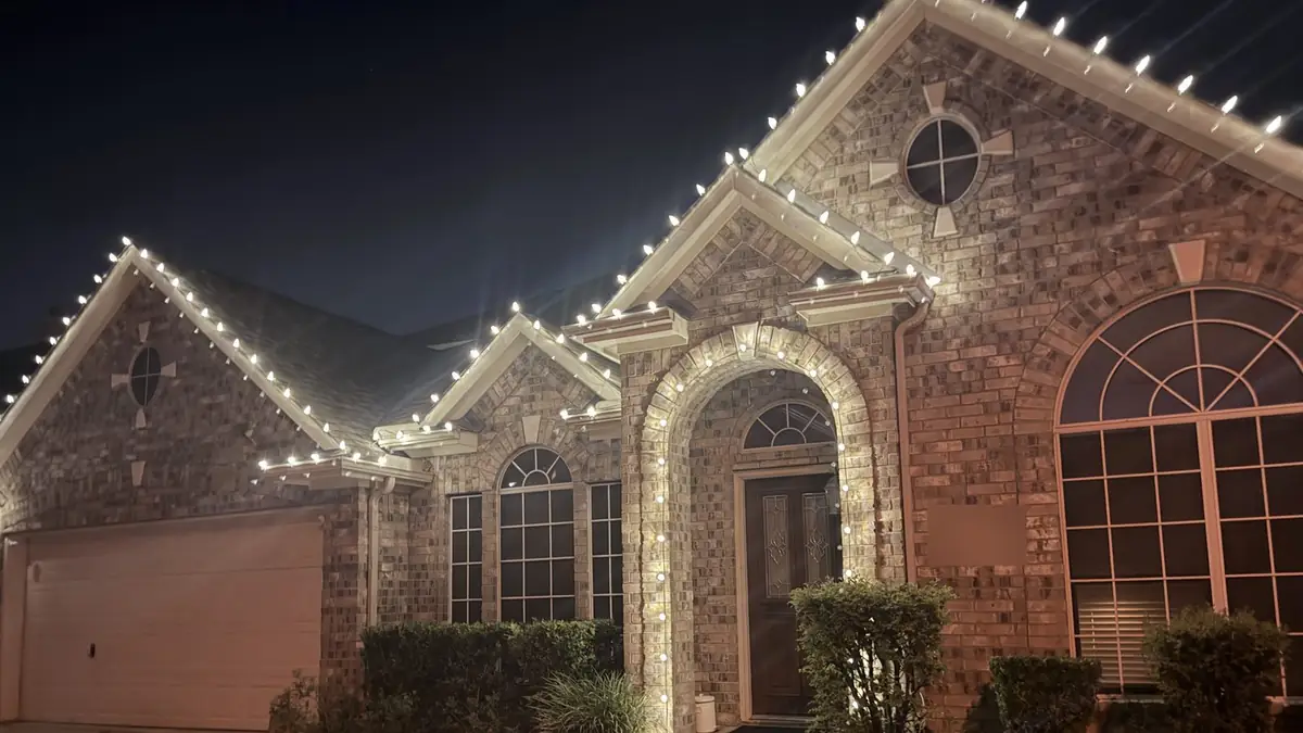 Brick home with warm white C9 Christmas lights on the roofline and arched entry, installed by QuietScapes